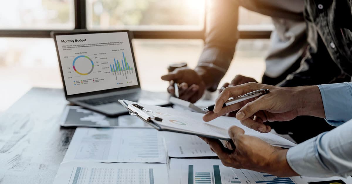 Two people reviewing financial papers and a laptop on the desk showing financial graph